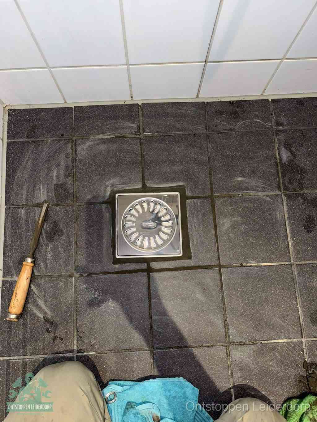 Een RVS doucheputje in een betegelde badkamervloer, zelf je badkamer ontstoppen in Leiderdorp
