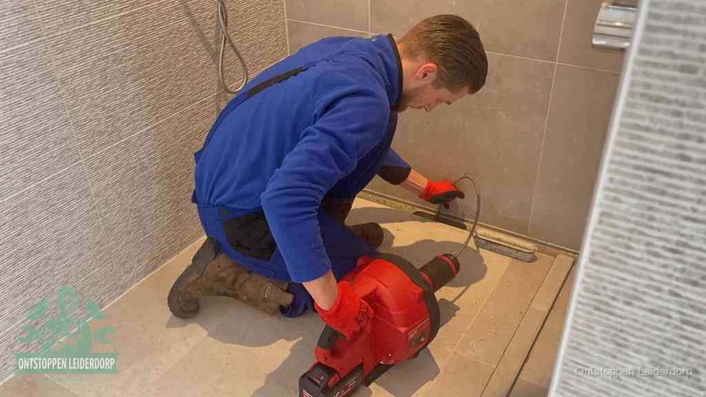 Een monteur ontstopt een langwerpige douchegoot met een elektrische veer, een doucheputje verstopt door haren en zeep in Leiderdorp