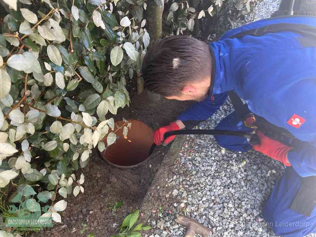 Een monteur voert een slang in een geopende rioolput in de tuin om het hoofdriool te ontstoppen in Leiderdorp